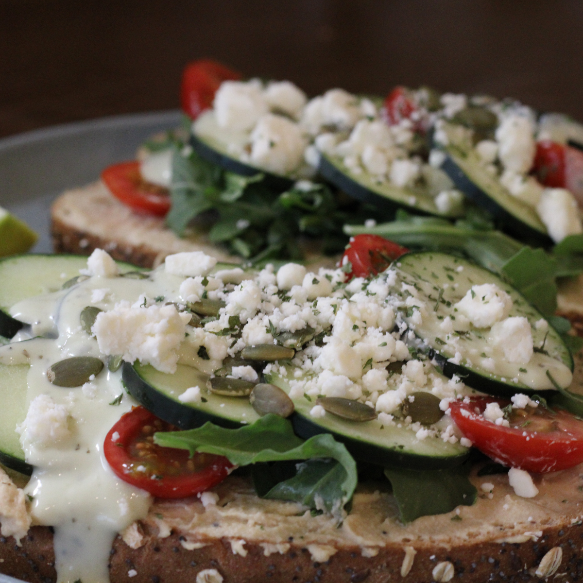Hummus toast topped with cucumber, tomato, feta and pepitas